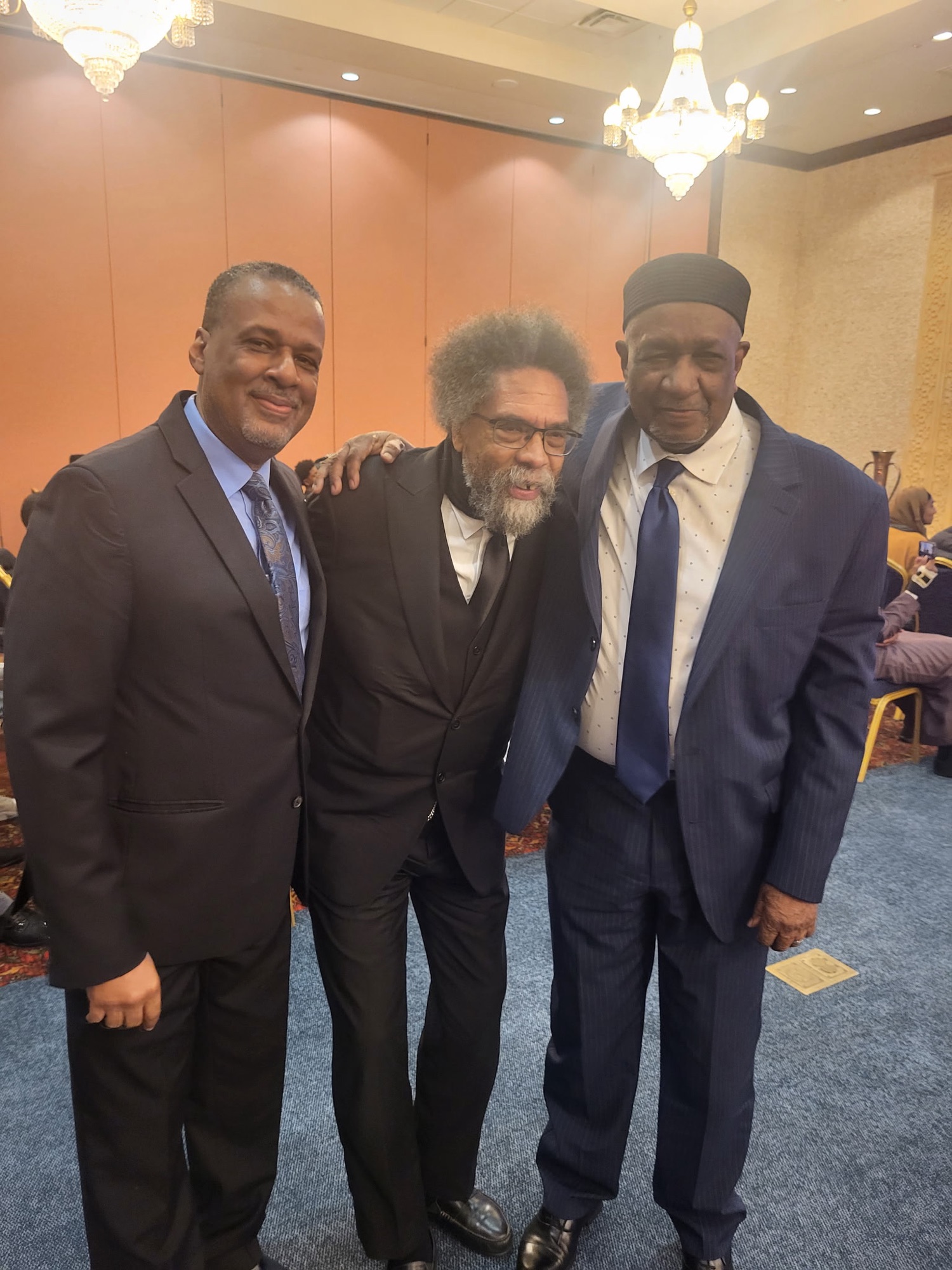 Three Men in suits standing arm in arm facing the camera. On the far right is Imam Darnell Karim and in the middle is Cornel West, the American philosopher, theologian, political activist, politician, social critic, and public intellectual. Next to him is Imam Karim's son Naeem Karim, professor.